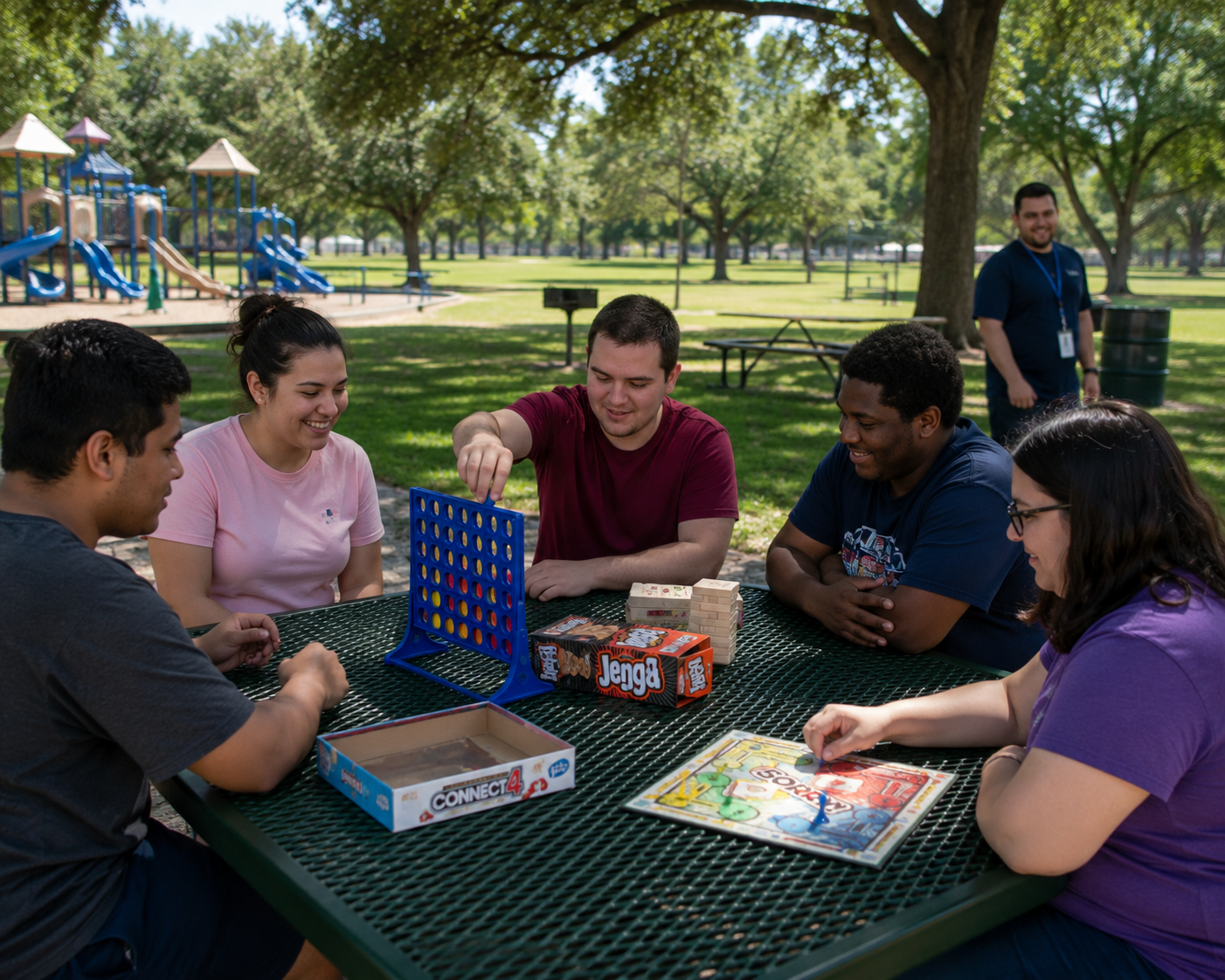 Young adults with disabilities playing Connect 4, Jenga, and Sorry at a park picnic table with a staff member nearby